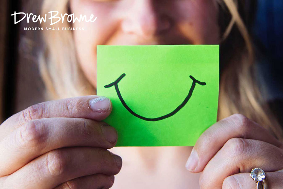 smiling face behind a green stickly note with as smiling face drawn in black ink