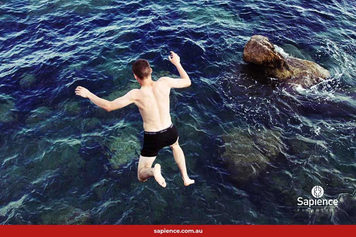 man jumping into deep water with rocks nearby