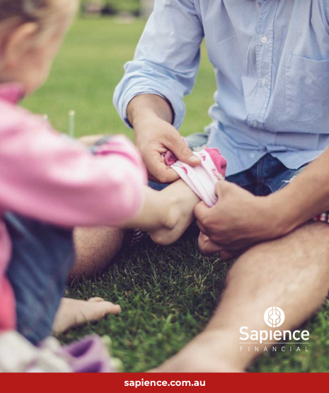 father putting sock on young child sitting on grass