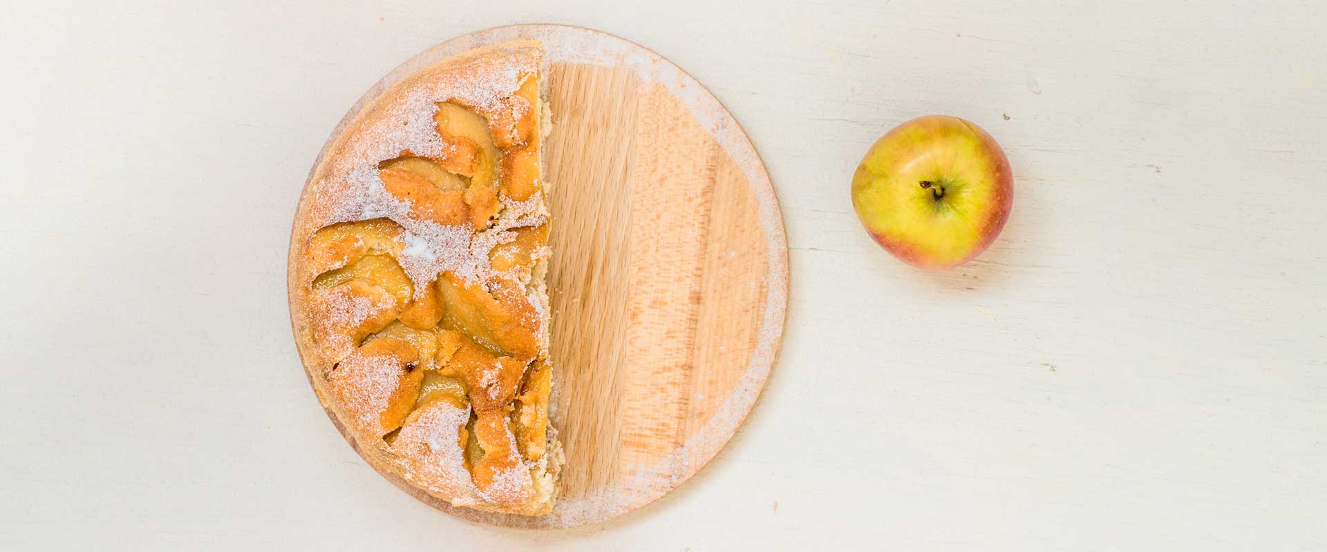 half an apple pie and a single apple on a wooden cutting board